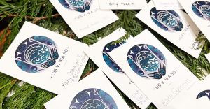 Honor cards displayed on cedar boughs with the blue and green logo for USvWA50 bear the hand-written names of Billy Frank Jr., Horton Capoeman, Howard Hudson and Lorraine Loomis.
